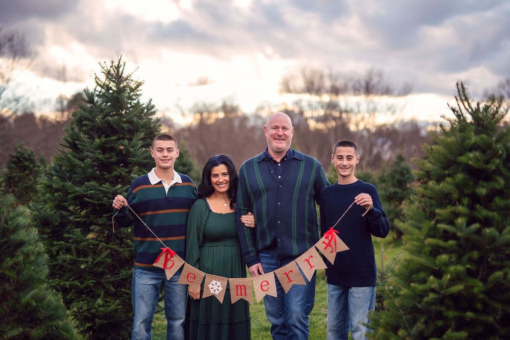 Family holding a holiday banner at a Christmas tree farm mini session