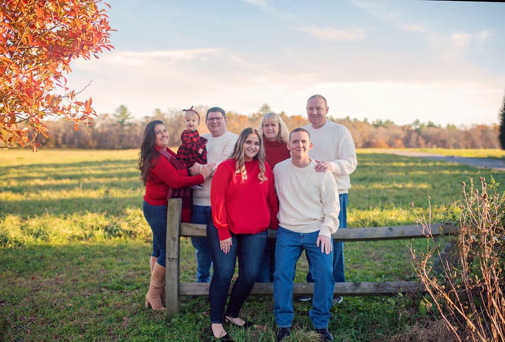 Extended family gathered at a split-rail fence with autumn foliage