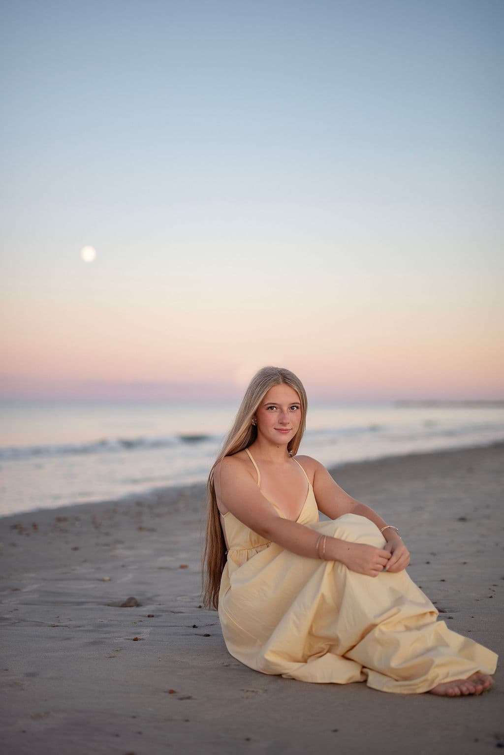 Senior girl in a yellow dress on the beach under a pastel evening sky with the moon rising