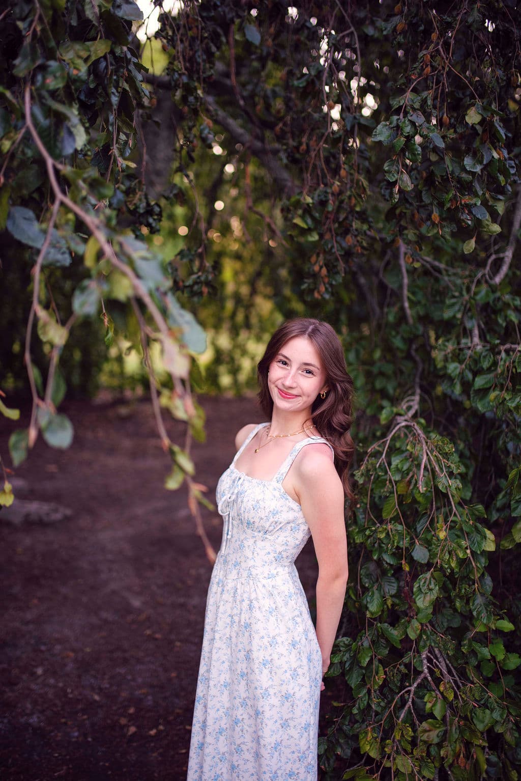 Senior girl in a white sundress under a leafy garden arbor