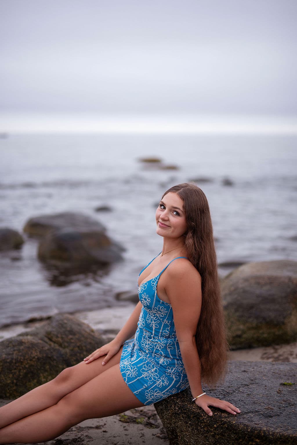Senior girl sitting on coastal rocks by the ocean at dusk