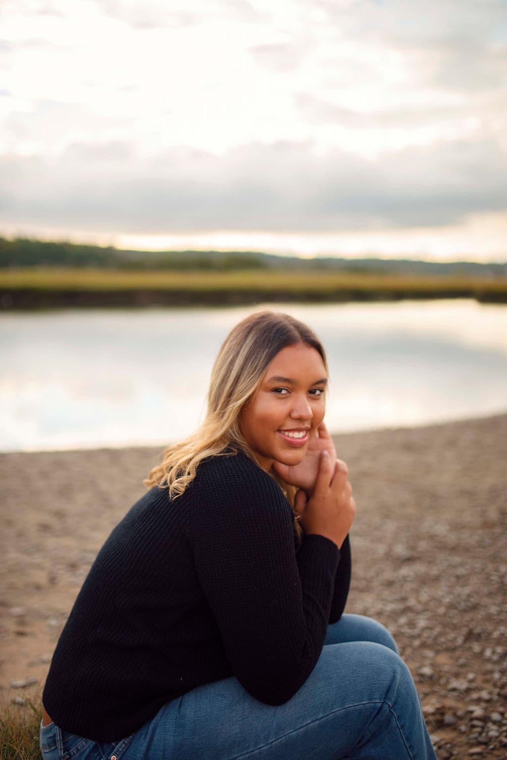 Smiling senior girl sitting on a sandy shoreline by the water