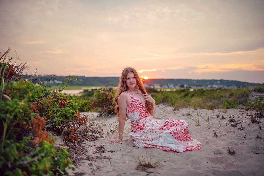 High school senior girl in a floral dress sitting in the dunes at sunset on the South Shore of Massachusetts