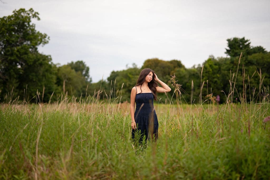 Senior girl standing in a tall-grass field edged by trees