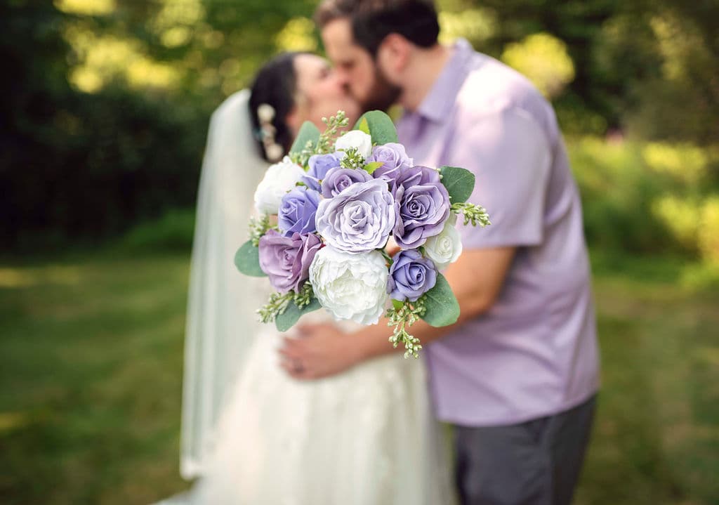 Bride and groom kissing behind a lavender bouquet